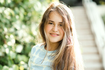 Beautiful teenage girl 14-15 year old with long blonde hair over green nature background close up outdoors. Looking at camera. Summer season.