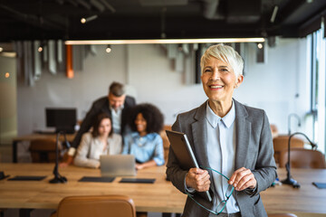 smile aged businesswoman executive stand in office and hold laptop