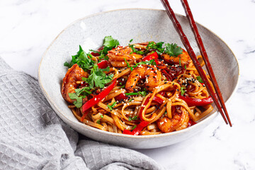 udon noodles, shrimp with vegetables and fresh herbs, in a bowl with chopsticks, light background, homemade, no people,