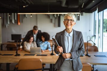 smile aged businesswoman executive stand in office and hold laptop