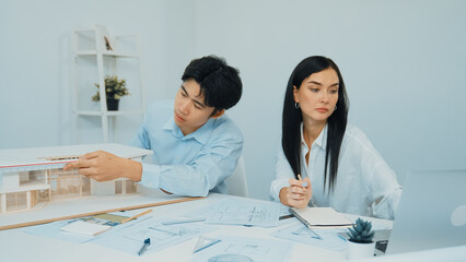 Professional male engineer measure house model by using ruler while beautiful cooperative coworker...