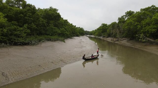 Khulna, Bangladesh &ndash; March 20, 2025: Local Fishermen Navigate a Wooden Boat Through a Narrow Channel of the Sundarbans Mangrove Forest