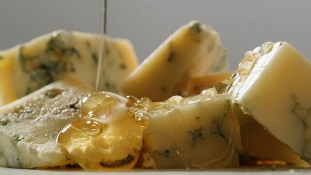 Tasty blue cheese with rosemary, honey and walnuts on white table, close up of Dorblu in cafe pouring in honey.