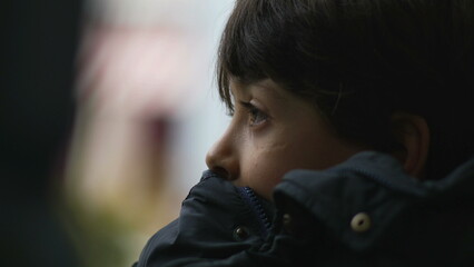 Obraz premium Close-up side profile of young boy resting his chin on jacket, gazing into distance with thoughtful expression, inside moving bus, staring at view passing by in contemplation