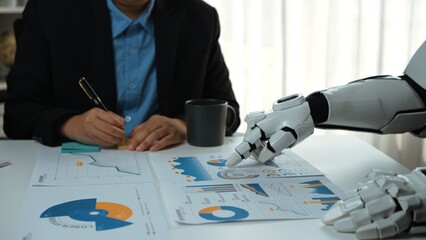A human and a robotic arm collaborate in a business meeting, analyzing financial reports and...
