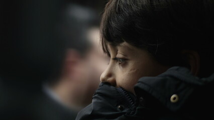 Close-up of young boy resting chin on jacket, staring at passing view outside moving bus, serious...