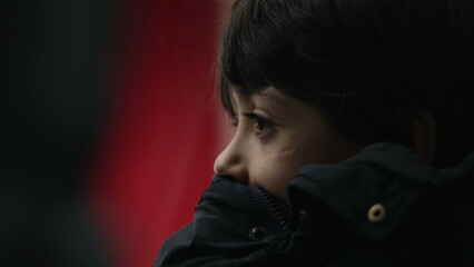 Close-up of young boy resting chin on jacket, staring at passing view outside moving bus, serious...