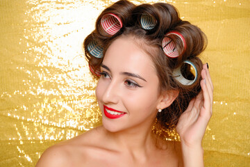 Beautiful girl in hair curlers isolated on gold