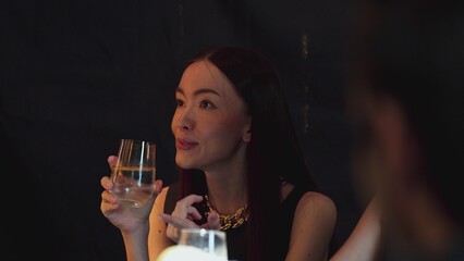 Portrait of beautiful woman making a toast and talking with friend drinking sparkling drink with sliced orange at luxurious counter beverage bar. Capturing essence social upscale at club. Vinosity.