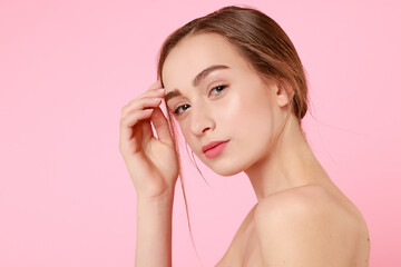 Beautiful young girl touching her perfect skin on pink background.