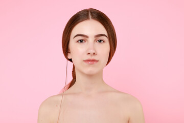 Beautiful young girl touching her perfect skin on pink background.