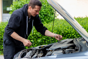 The car broke down while traveling. A frustrated man near a broken car with an open hood far outside the city.  A young guy looks under the hood of a car.