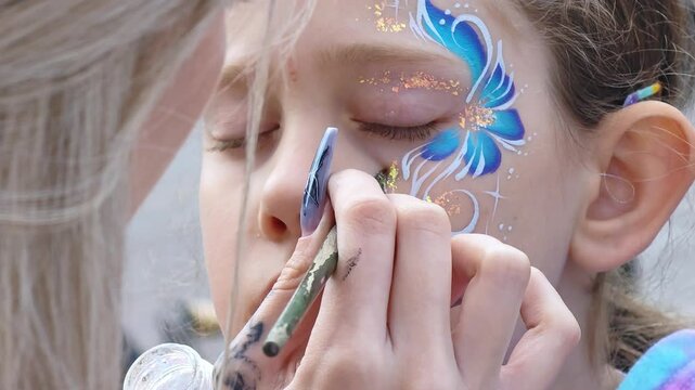 Painter hand draws face painting to little girl. Aqua makeup. Children party.