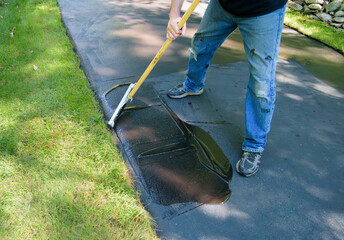 A man spreading blacktop sealer along the edge of the driveway
