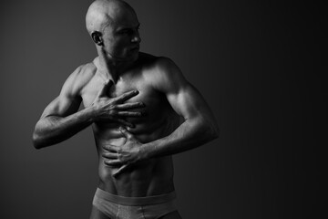 Black and white image of a muscular man touching his chest with a serious expression, showcasing strength and emotion. A dramatic light highlights his physique.