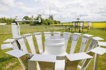 Close-up of a rain gauge at a weather station used for measuring precipitation in a rural field.