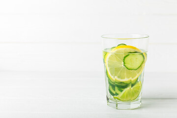 Cucumber water with lemon, lime and mint on a wooden table. Water infused with sliced ​​cucumber in a drinking glass. Tonic refreshing drink. Cucumber lemonade.Summer natural cooling drink.Copy space
