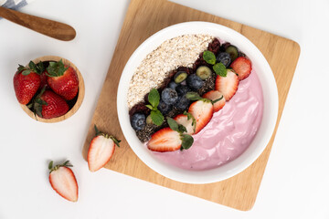 Presented by fruits putting yogurt toppings with strawberry, berry, oats, raisins and chia seed decorated by peppermint in white blow. Pink background. Set of healthy dairy product choice. Pecuniary.