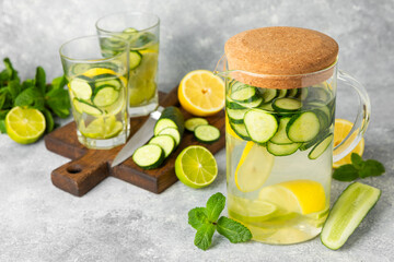 Cucumber water with lemon, lime and mint on a wooden table. Water infused with sliced ​​cucumber in a drinking glass. Tonic refreshing drink. Cucumber lemonade.Summer natural cooling drink.Copy space