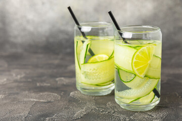 Cucumber water with lemon, lime and mint on a wooden table. Water infused with sliced ​​cucumber in a drinking glass. Tonic refreshing drink. Cucumber lemonade.Summer natural cooling drink.Copy space