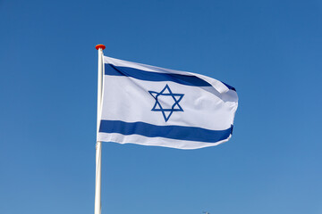 The national flag of Israel, featuring the Star of David and blue stripes, proudly waves against a clear blue sky, symbolizing national identity.