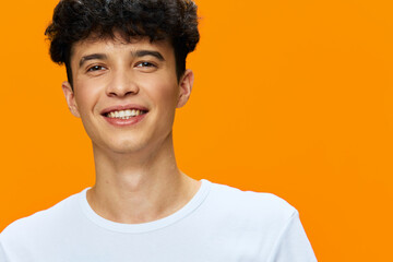 smiling man with curly hair wearing white t-shirt standing against vibrant orange background, youthful expression, casual style, bright and cheerful portrait