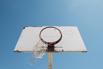 An abandoned basketball court. The backboard is discolored and the net of the basket is broken.