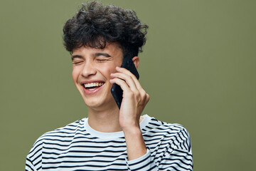 smiling man talking on smartphone with curly hair wearing striped shirt, happy expression, olive...