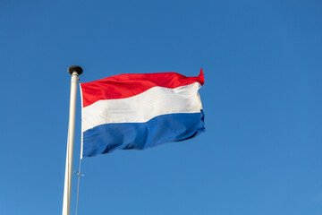 The vibrant red, white, and blue flag of the Netherlands proudly waves against a clear, azure sky, symbolizing national pride and freedom.