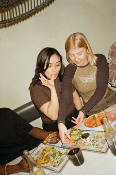 Young woman licking fingers while eating fast food with friends at restaurant