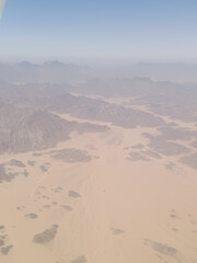 Aerial view of rugged desert mountains and sandy valleys under hazy sky