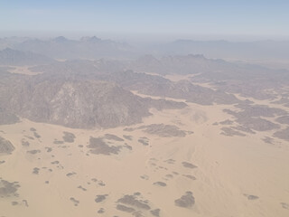Aerial view of rugged desert mountains and sandy valleys under hazy sky