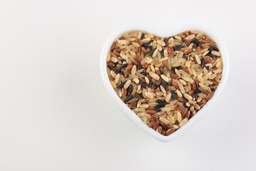 Raw dry mix of different rice varieties in heart shaped white bowl on white background isolated