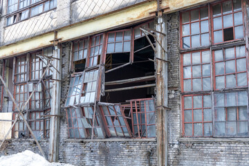 Exterior of old abandoned factory with shattered windows, weathered brick wall, and rusty beams,...