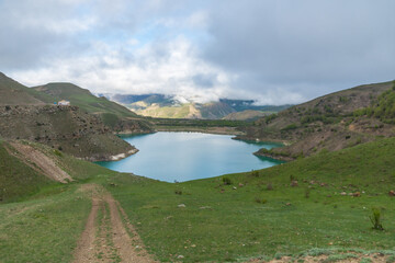 Lake Gizhgit in Kabardino-Balkaria, Russia, surrounded by rolling green hills and partially covered by low-hanging clouds