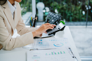 A young adult woman sitting at a table at home, paying bills through an e-bank on a digital tablet, calculating expenses with a calculator, and using modern technology to manage finances and perform o