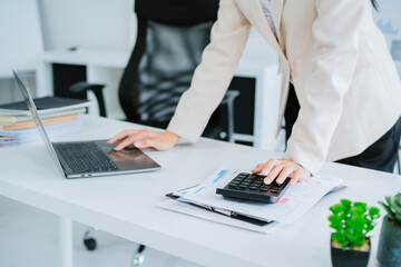 Asian businesswoman working on laptop in bright white modern office.