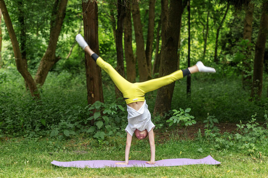 Child doing handstand split on yoga mat outdoors