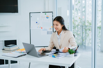 Image of beautiful Asian woman sitting and working with laptop, documents, graphs in office.