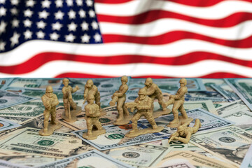Militarism and the US economy. Toy soldiers stand on US dollars against the background of the US flag, symbolising the influence of military spending and the economy on world politics.