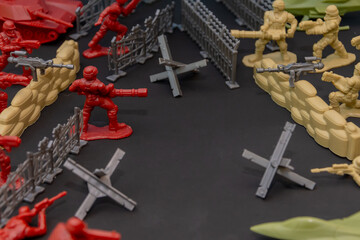 A battle scene with toy soldiers. Plastic soldiers, fortifications, barriers and tanks depict military conflict on a black background, confrontations and strategies.