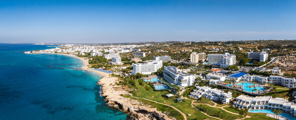 Aerial view of Ayia Napa, Cyprus, showing turquoise waters, sandy beaches, luxury resorts, Nissi Beach, Landa Beach, and urban greenery.