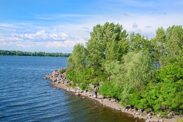 Picturesque view from the bridge of the rocky shore of the strait with lush green trees by the calm...