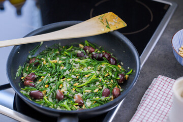 The salty vegetable agretti, friar´s beard, in pan on oven with onions, pine nuts and olives