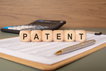 wooden cubes spelling PATENT on a financial document with a pen and calculator in the background