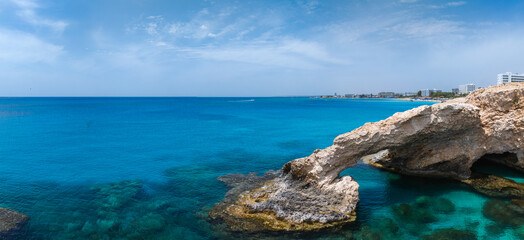 Coastal view in Ayia Napa, Cyprus, with a natural rock Love arch over clear turquoise waters, sandy beaches, and luxury resorts along the shoreline.