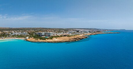 Fototapeta premium Aerial view of Ayia Napa, Cyprus, showing turquoise waters, Nissi Beach, luxury resorts, sandy beaches, rocky outcrops, and urban areas in sunlight.