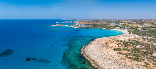 Aerial view of Ayia Napa, Cyprus, showing Nissi Beach, turquoise waters, sandy coastline, rocky outcrops, luxury resorts, and small boats in the sea.