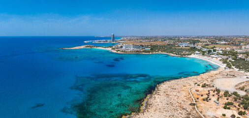 Aerial view of Ayia Napa, Cyprus, showing Nissi Beach, turquoise waters, sandy coastline, rocky outcrops, luxury resorts, and small boats in the sea.