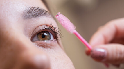 Caucasian woman brushing her eyelashes after lamination. 